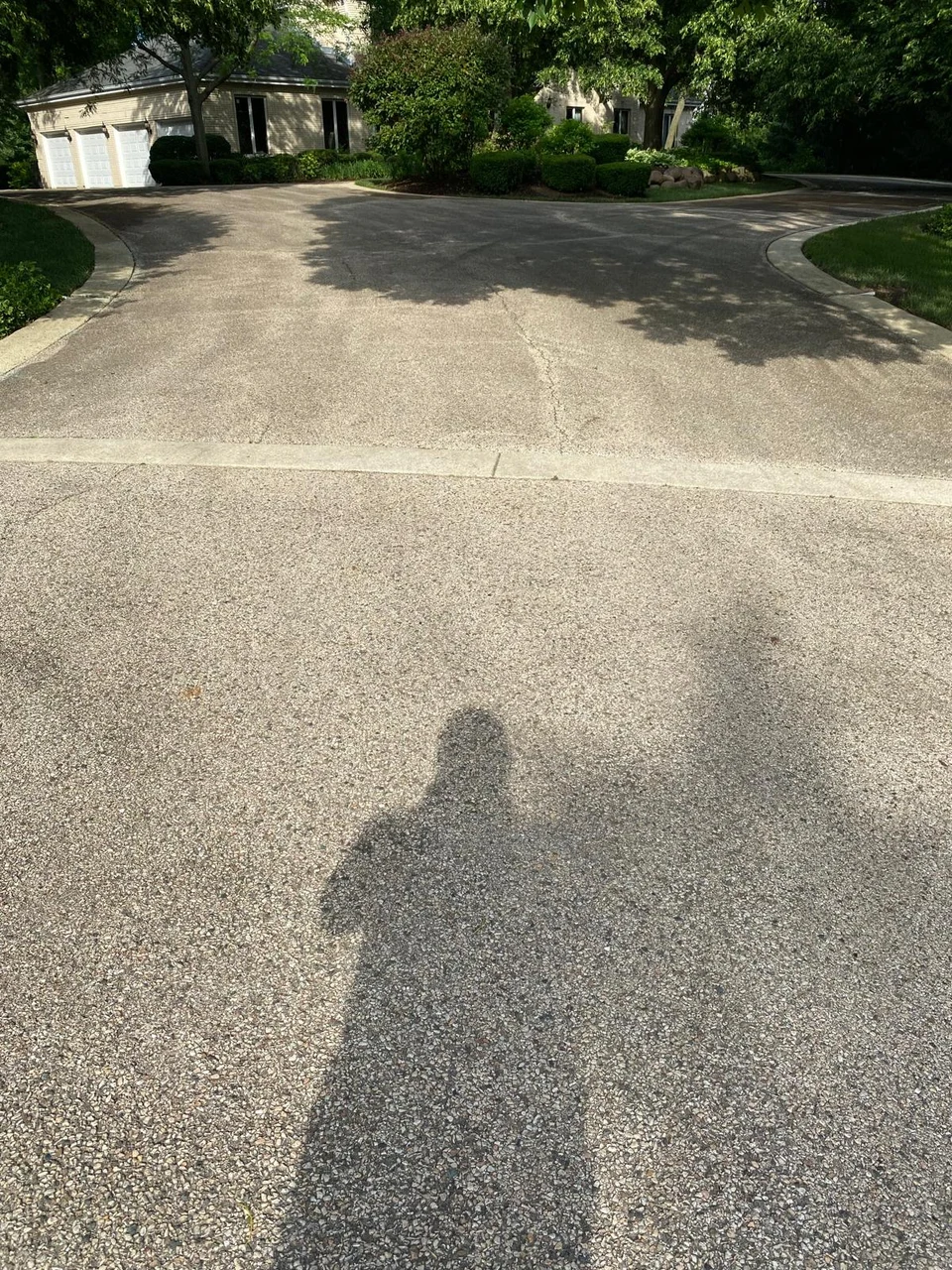 Circular driveway before sealcoating, with faded asphalt, a light stone strip, and a planted island in front of a light-colored house