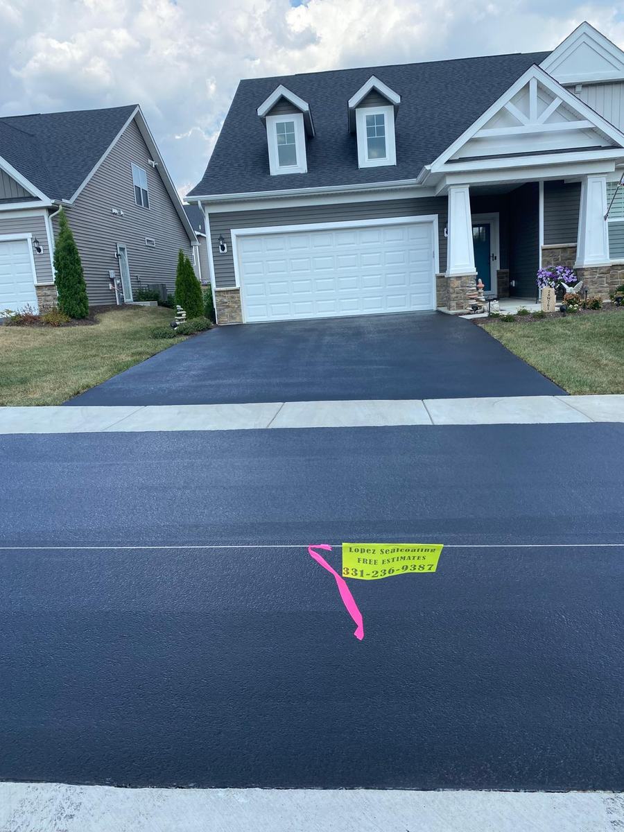 Sealed driveway in front of a home with a white garage door and blue-gray roof